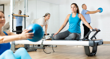 Focused young girl performing set of pilates exercises on reformer in modern fitness studio..