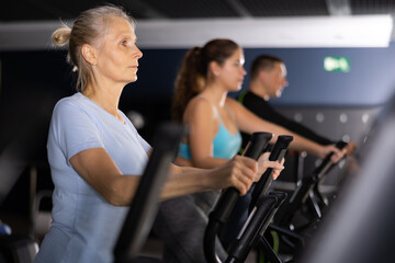 Fototapeta na wymiar Elterly fitness woman in sportswear doing cardio training on ellipsoid in gym