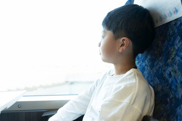 電車の窓から外を見る小学生の男の子