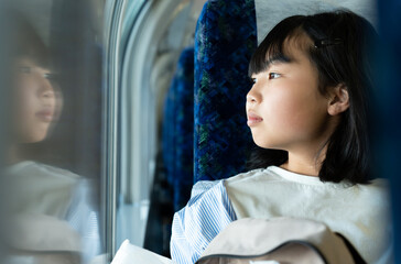 電車の窓から外を見る10代の女性