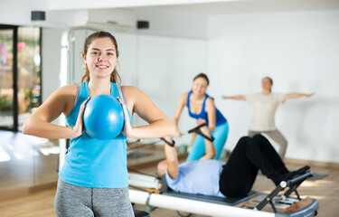 Fototapeta na wymiar Smiling young girl doing chest muscles exercises with bender ball during workout in pilates studio