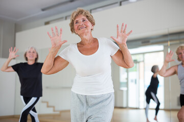 Fototapeta na wymiar Portrait of mature energetic woman and people practicing active dancing in the studio at a group lesson