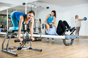 Peaceful middle-aged female in activewear concentrating on stretching exercise on Pilates chair equipment in gym