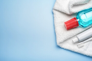Obraz na płótnie Canvas Toothbrush with paste tube, terry towel and mouthwash bottle on blue background. Top view, copy space.
