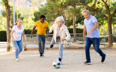 Joyful middle aged mixed-race people having good time together while playing football in public park on a sunny day