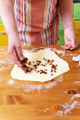 Woman baker lays raisins in pastry dough for making buns at home kitchen.