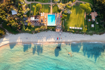 Aerial view of empty sandy beach, sea with azure water and waves, green palm trees and meadows, blue pool at sunset in summer. Sardinia, Italy. Tropical landscape. Nature. Top down view. Drone view