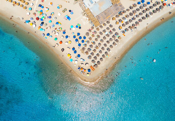 Aerial view of colorful umbrellas on sandy beach, people in blue sea at summer sunny day. Tuerredda...