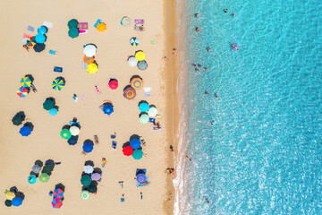 Aerial view of colorful umbrellas on sandy beach, people in blue sea at summer sunny day. Sardinia,...