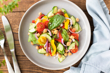 Vegetarian vegetable salad with chickpeas, tomatoes, red onions, cucumbers and lettuce. Vegetarian food rich in protein and fiber. Vegetable salad on wooden table top view