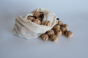 Shelled walnuts falling from a white cloth bag on a white background. 
