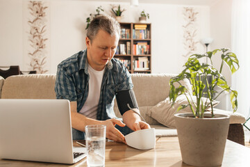 A man measures his blood pressure at home using a tanrometer and a measuring cuff. The concept of...