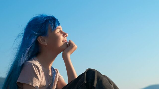 Blue teen with dreaming eyes on beach. A colorful fashioned teen girl with dreaming eyes have a rest on the beach against clear sky.