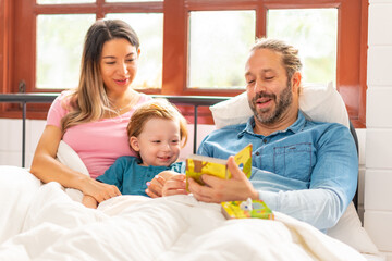 Obraz na płótnie Canvas Happy Caucasian father and mother playing toy with little baby son on the bed in bedroom. Parents and child boy kid enjoy and fun indoors lifestyle together at home. Family relationship concept.