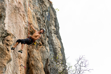 Young Asian man climber climbing on rocky coastline at tropical island in sunny day. Handsome guy...