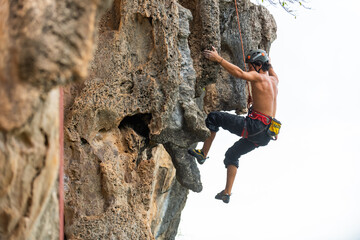 Young Asian man climber climbing on rocky coastline at tropical island in sunny day. Handsome guy...