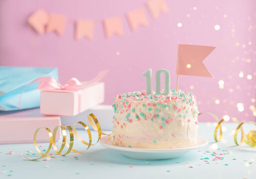 Festive cake with number 10 on background of festive pink wall with gifts and flags in serpentine.