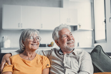 Dreamy middle aged senior loving retired family couple looking in distance, planning common future or recollecting memories, enjoying peaceful moment relaxing together on cozy sofa in living room.