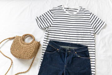 Blue jeans, t shirt, bag and white sneakers on white bed. Trendy clothes. Women's casual spring summer outfit. Fashion concept. Flat lay, top view
