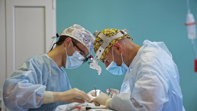 Two doctors with headlights cooperate in the surgery room. Male doctors perform thyroidectomy.