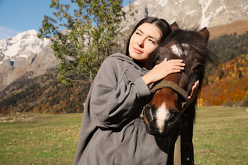 Young woman hugging horse in mountains on sunny day. Beautiful pet