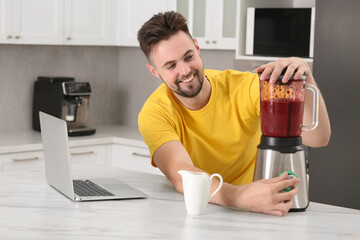 Happy man making smoothie while watching cooking online course in kitchen. Time for hobby