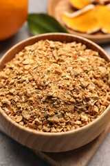 Bowl of dried orange zest seasoning and fresh fruits on light grey table, closeup