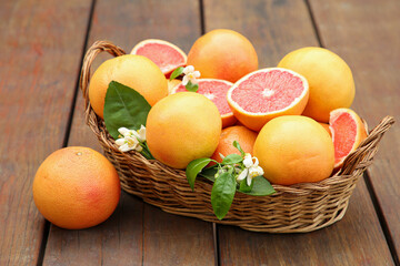 Wicker basket with fresh grapefruits and green leaves on wooden table