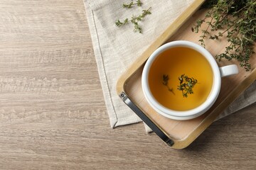 Cup of fresh thyme tea on wooden table, flat lay. Space for text