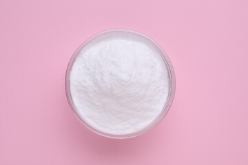 Bowl of sweet powdered fructose on pink background, top view