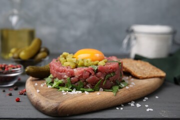 Tasty beef steak tartare served with yolk, pickled cucumber and other accompaniments on grey wooden table