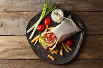 Delicious pita wrap with prosciutto, vegetables and potato fries on wooden table, top view