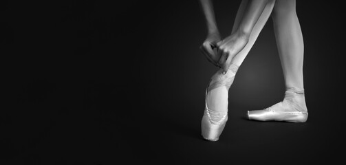 Young ballerina tying pointe shoes, closeup. Black and white effect. Banner design with space for text