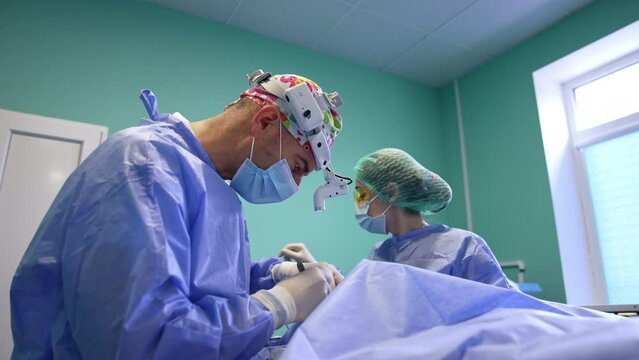 Doctor carefully uses scalpel to make an incision. Nurse in yellow protective goggles assisting the surgeon.