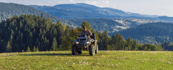 A man driving a quad ATV motorcycle through beautiful meadow landscapes