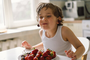 Cute beautiful little boy eating fresh cherry and strawberry. Healthy food, childhood and development. Happy kid at home.