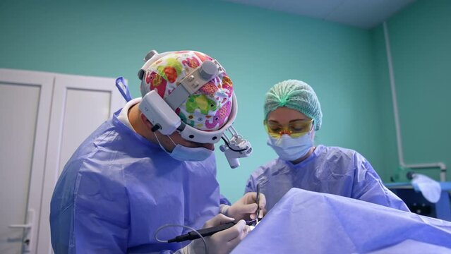 Thyroidectomy in modern clinics. Surgeon wearing headlight uses electric device. Assisting nurse watching the procedure.