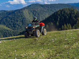 A man driving a quad ATV motorcycle through beautiful meadow landscapes