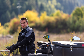 A man in a forest posing next to a quad and preparing for ride