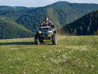 Fototapeta premium A man driving a quad ATV motorcycle through beautiful meadow landscapes