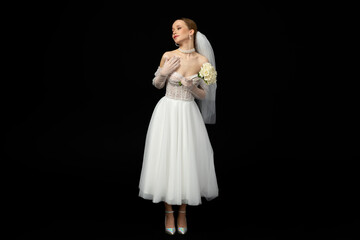 A beautiful charming girl, the bride in a luxurious and elegant white wedding dress, poses tenderly with a graceful bouquet of white roses. Isolated on a black background.