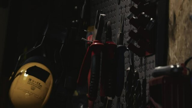 The hand hangs the pliers on the binder in the workshop among other tools