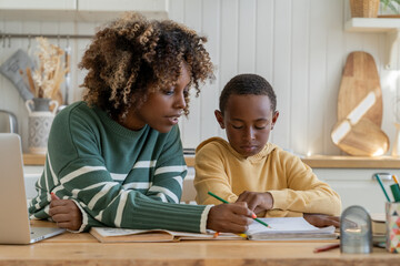 Focused biracial mother explaining difficult school task to attentive son for effective learning. African American personal tutor woman and little schoolboy sit at desk in home kitchen study together - Powered by Adobe