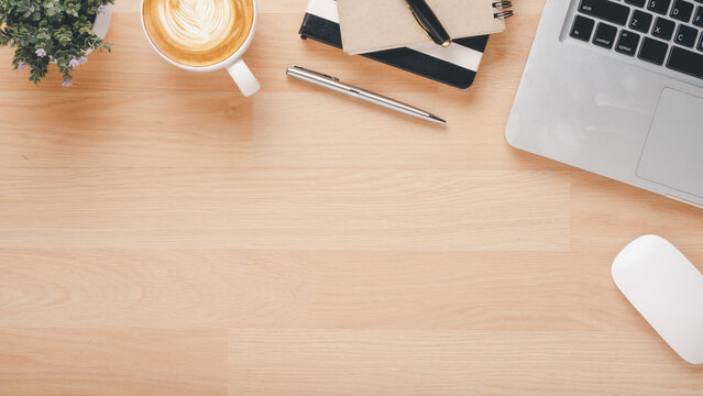 Office wooden desk workplace with laptop computer, mouse, notebook, pen and cup of coffee, Top view flat lay with copy space.