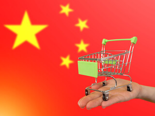 Trolley from supermarket. Chinese flag. Hand with miniature shopping cart. Concept ordering goods in China. Buying goods in PRC. Metaphor of import from China. Shopping in people's republic of China