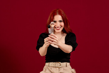 Woman smiling while holding makeup brushes standing against an isolated background.