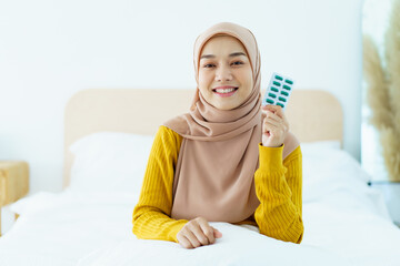 Asian young muslim woman showing a pill and water bottle, muslim woman taking a pill capsule. Health care and wellness in diverse ethnicity people and religious concept.