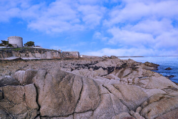 Fototapeta na wymiar Rock formations on the coast at Sandycove, Ireland, with the Martello Tower where James Joyce stayed in the background