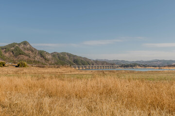 Landscape of field in rural area with lake and bridge in distance..