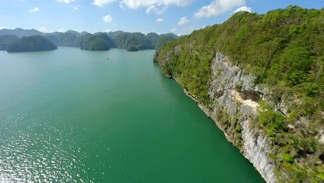 Aerial fpv flight Along rocky coastline with green plants and green water during summer day - bay of Samana, Domin ican Repilic